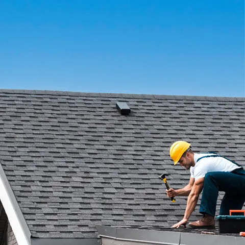Roofer in a hard hat repairing a shingle roof